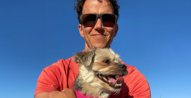 An adorable image of a small Morkie, Charlotte, smiling while being held by her owner. The scene captures the essence of trust and playfulness, emphasizing the tiny size of the dog compared to the human, highlighting the theme of trust without fear.